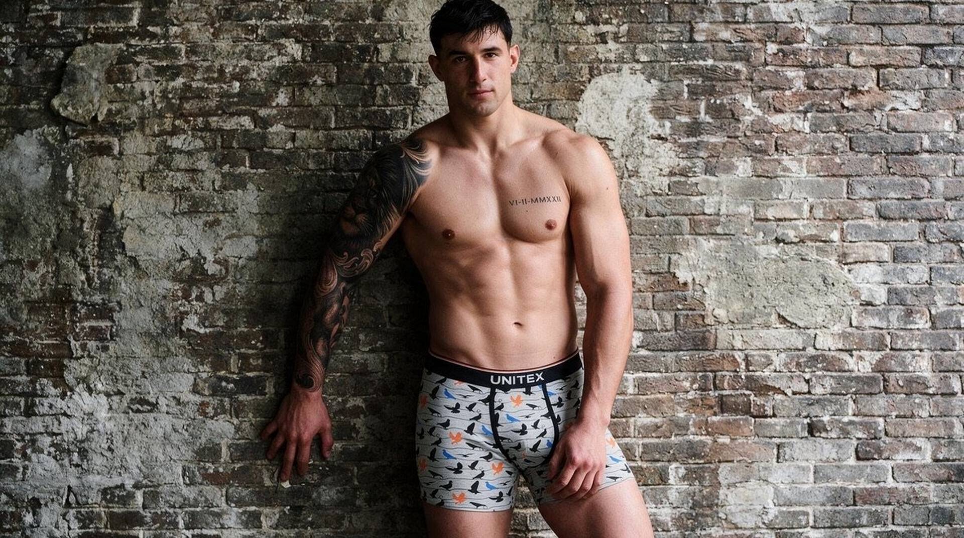 Model leaning on a brick wall wearing patterned Unitex boxer briefs — hero image